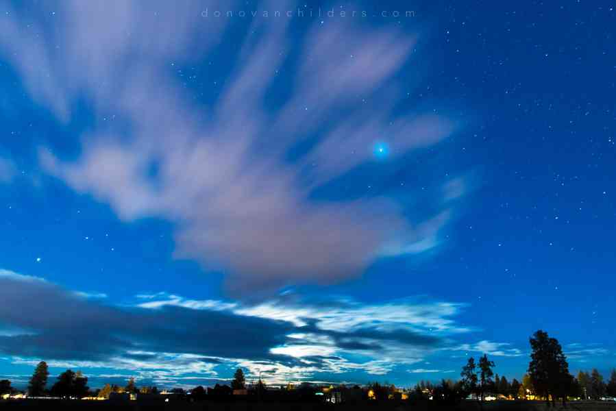 Moon behind the clouds, stars and planet Jupiter to the right of center